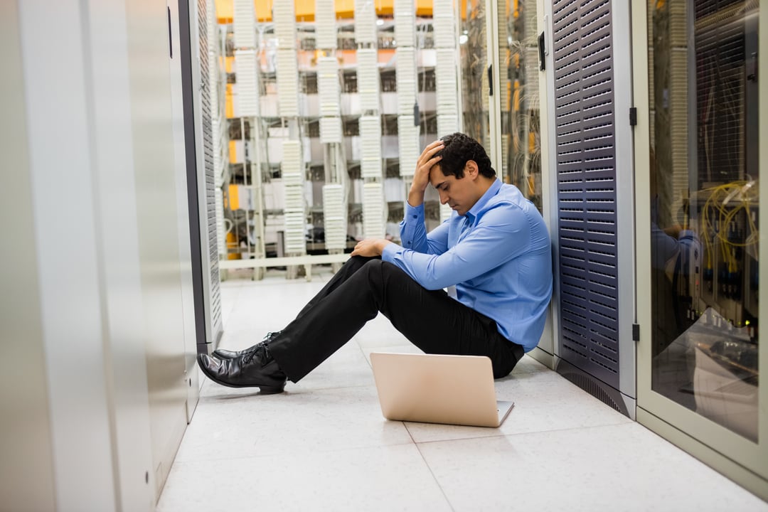 Stressed IT technician sitting on the floor of a server room.